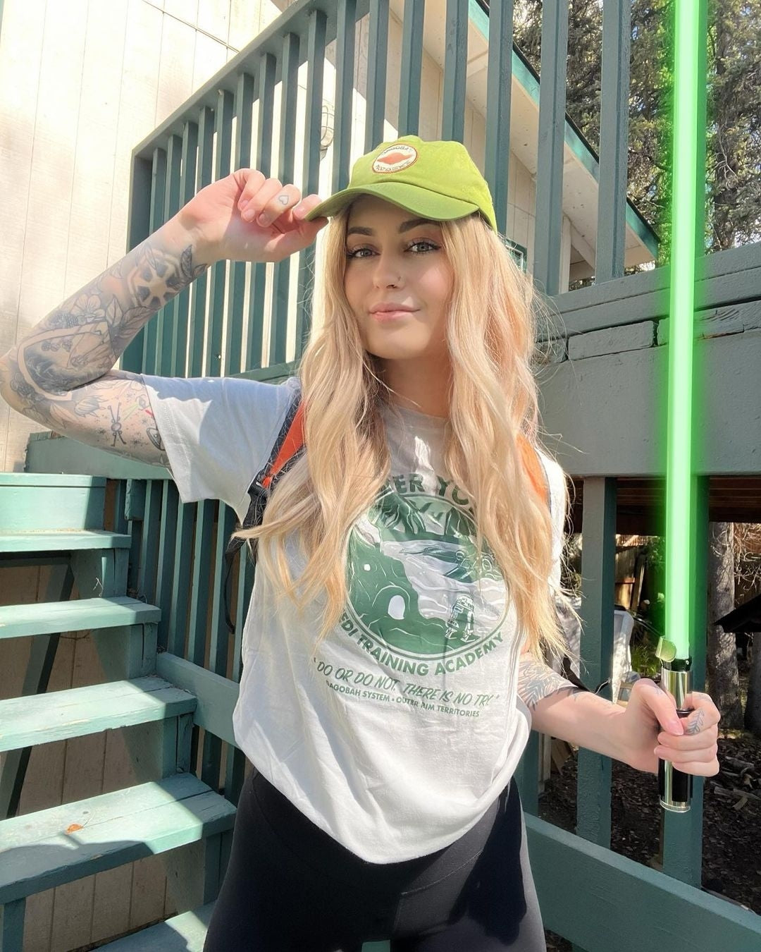 Person wearing a green cap and white t-shirt with graphics, holding a green light saber.