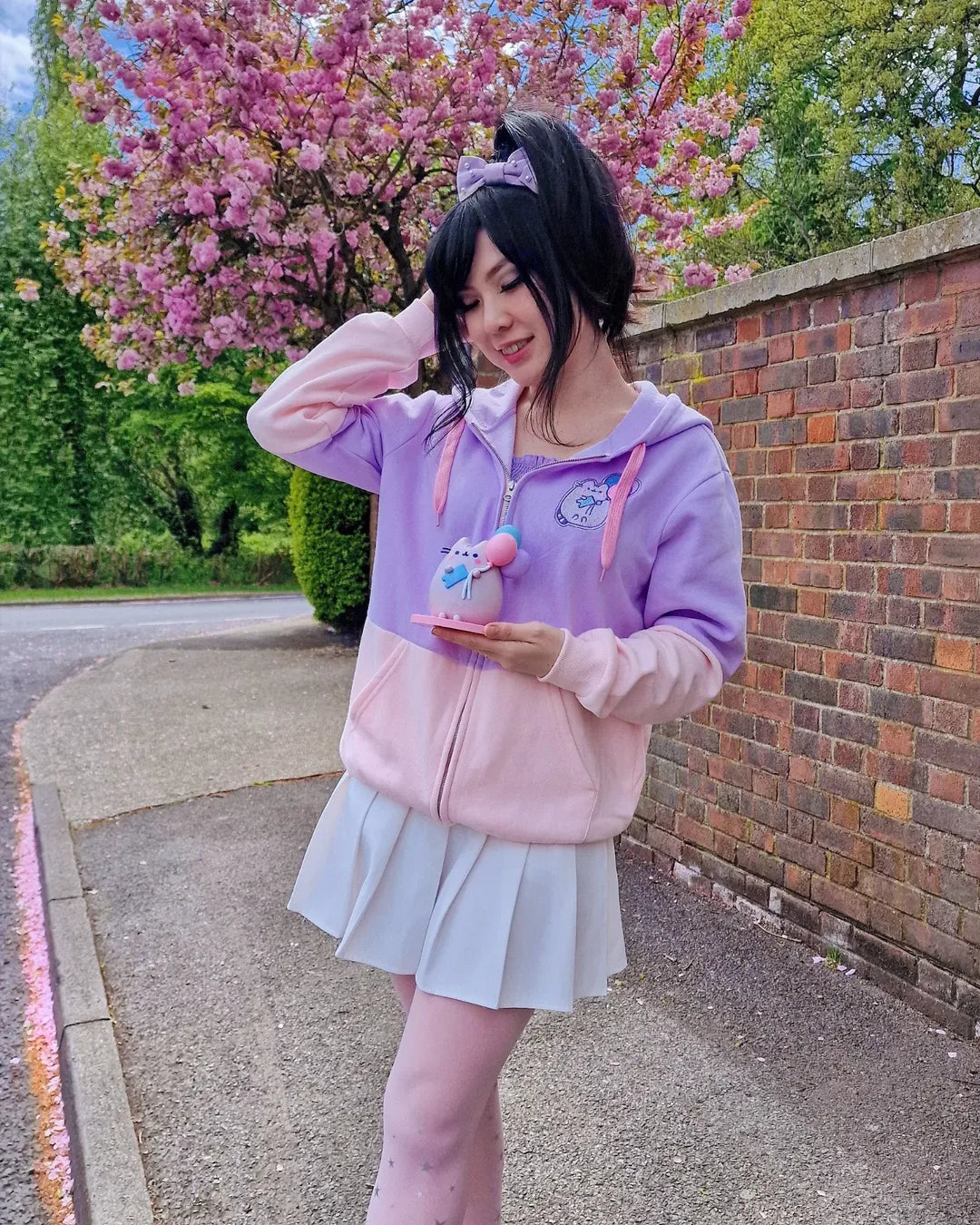Person wearing a pastel pink hoodie and skirt standing in front of cherry blossom trees.
