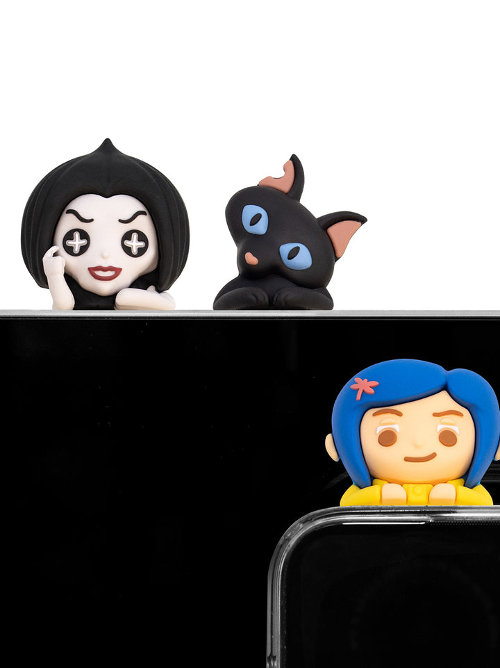 Three small character figurines displayed on a black surface against a white background: a black-haired pale face figure, a black cat with blue eyes, and a blue-haired girl figure with a yellow top peeking over a black phone or frame.