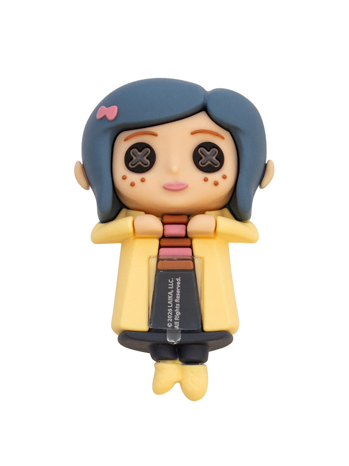 A collectible vinyl figure of the doll version of Coraline, featuring her signature blue hair, yellow coat, and black pants, shown on a plain white background.