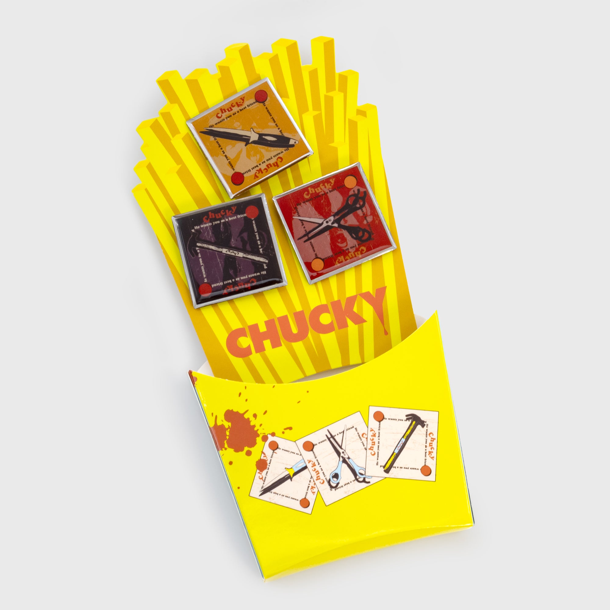 chucky freakie meal pin set inside of french fries container. 3 pins. image on each pin: knife, hammer, scissors. TextL chucky he wants you as a best friend