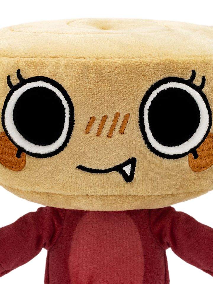 A close-up of a plush toy with a round beige head resembling a bread roll, featuring large cartoon eyes, embroidered facial details, and a dark red body.