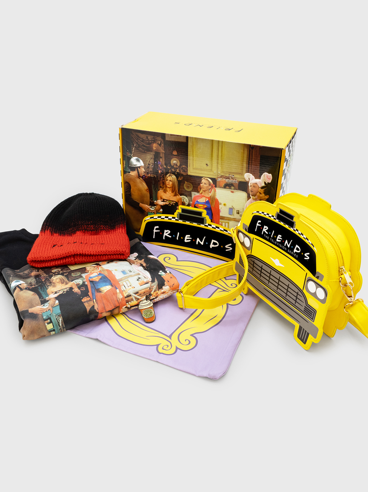 Collection of 'Friends' themed items including a yellow crossbody bag, plush pillow, and beanie on a white background.