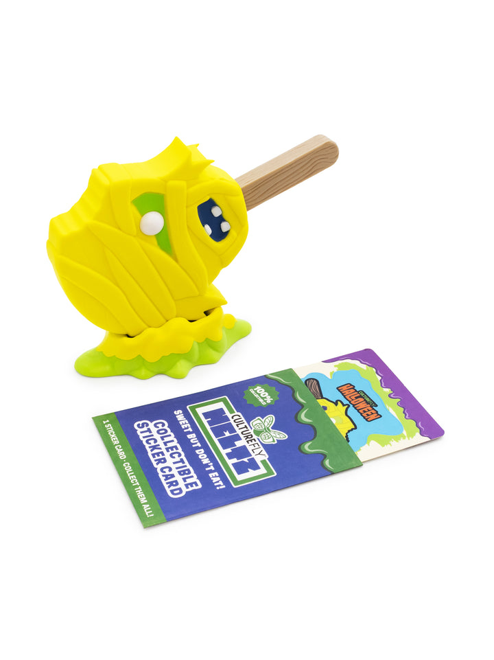 A yellow mummy stick toy with a wooden handle, shown next to a colorful collectible sticker card on a white background.