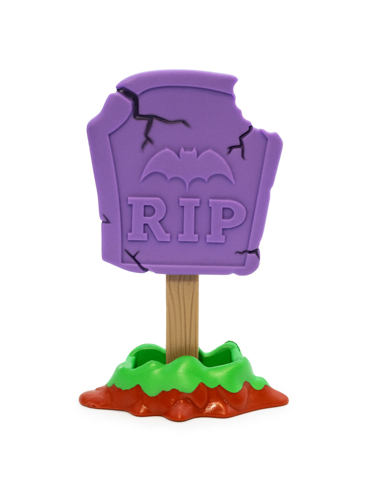 A Halloween tombstone sign stand with a purple RIP plaque, black cracks, a bat silhouette, and a wooden stake set in a green and orange fake ground base, isolated on a white background.