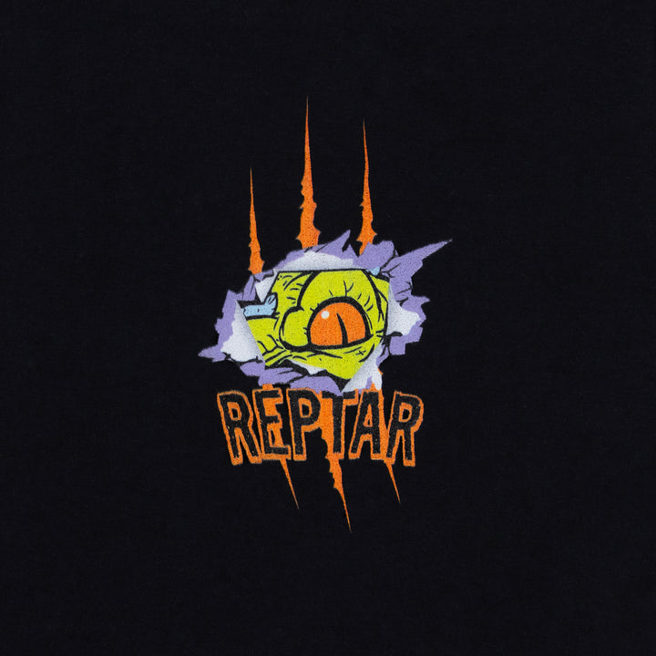 james groman reptar black tee close up of front left pop area design. Image: reptar dinosaur's eye peeking out of a hole made with a slash. text: reptar.