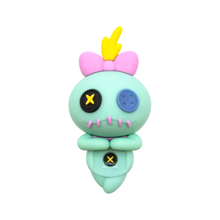 A mint green plush toy figure with a pink bow, yellow hair, and mismatched black and blue buttons on its eyes, shown against a plain white background.