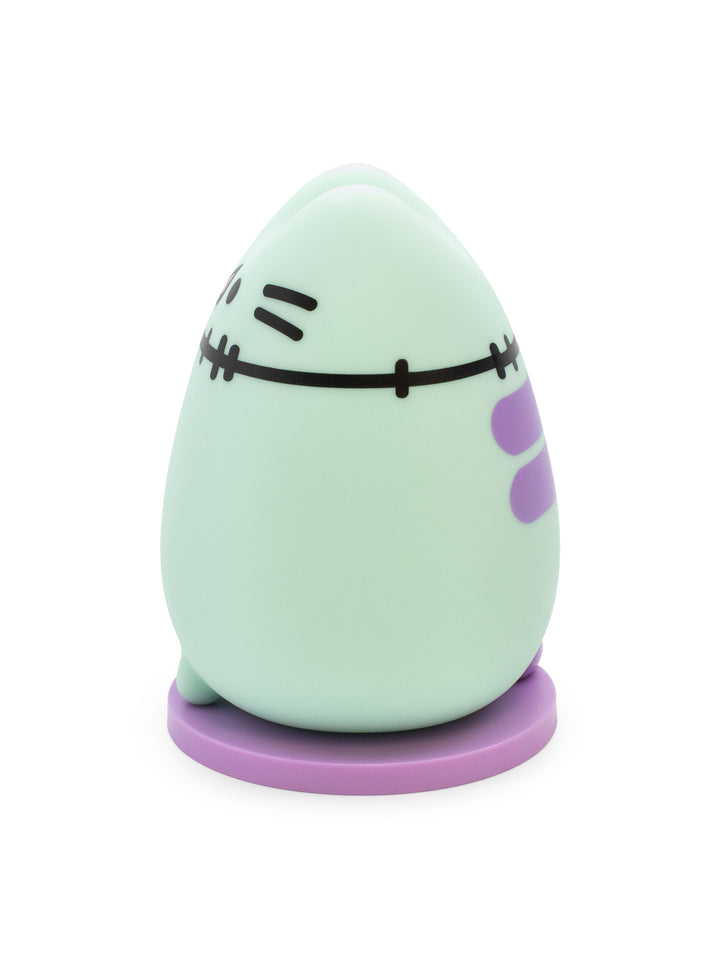 A cute, rounded zombie-like figurine in mint green with a purple base and purple side details, featuring stitched facial features, on a plain white background.