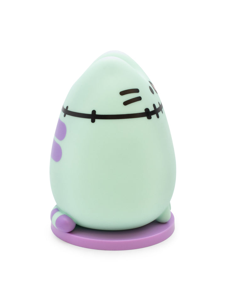 A cute, egg-shaped character figurine in a pale mint green color with purple accents and black stitched facial features, standing on a round purple base against a white background.