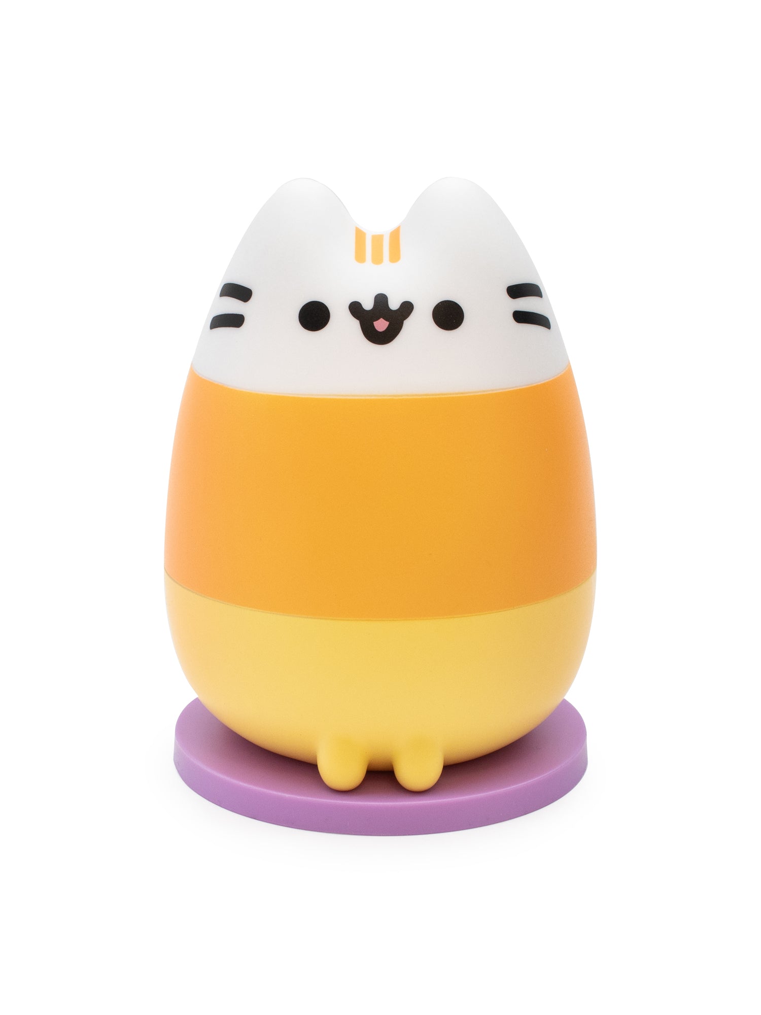 A Pusheen the Cat character figurine styled like a candy corn, featuring a white top section with black whiskers and eyes, a middle orange band, a yellow bottom section, and standing on a purple circular base.