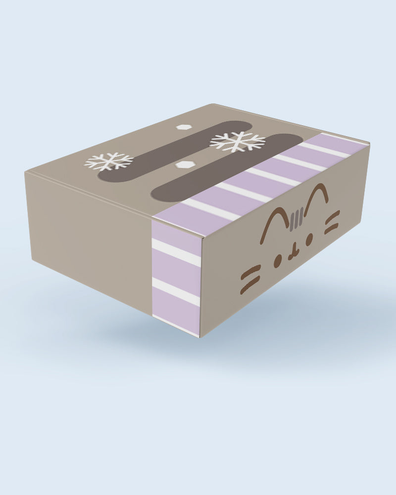 A rectangular gift box with a light brown base, decorated with lavender and white stripes, dark brown handles, white snowflakes, and a cartoon cat face on the side, shown against a light blue background.