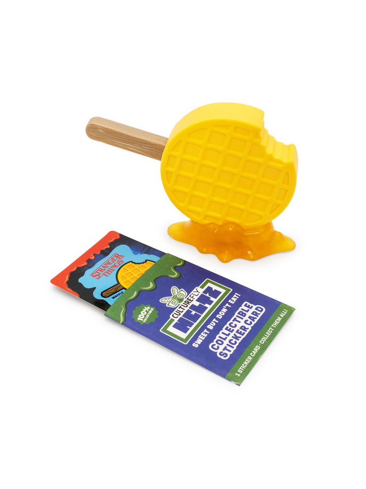 Yellow waffle with a wooden stick and a package of stickers on a white background