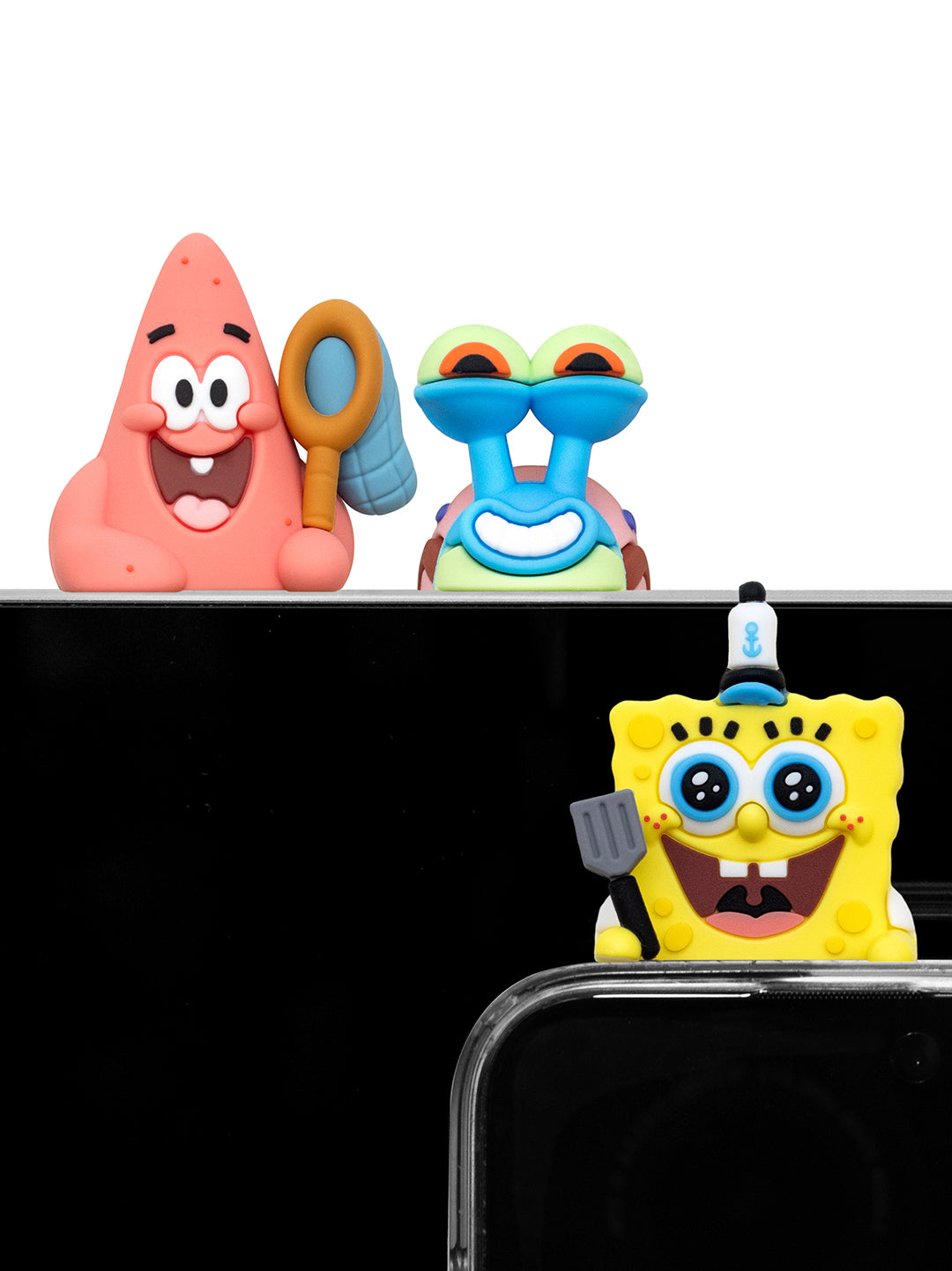 Three SpongeBob-themed phone accessories are shown: a Patrick Star figure holding a fishing net, Gary the Snail figure, and a SpongeBob character figure with a small blue hat, all positioned above a black smartphone screen.
