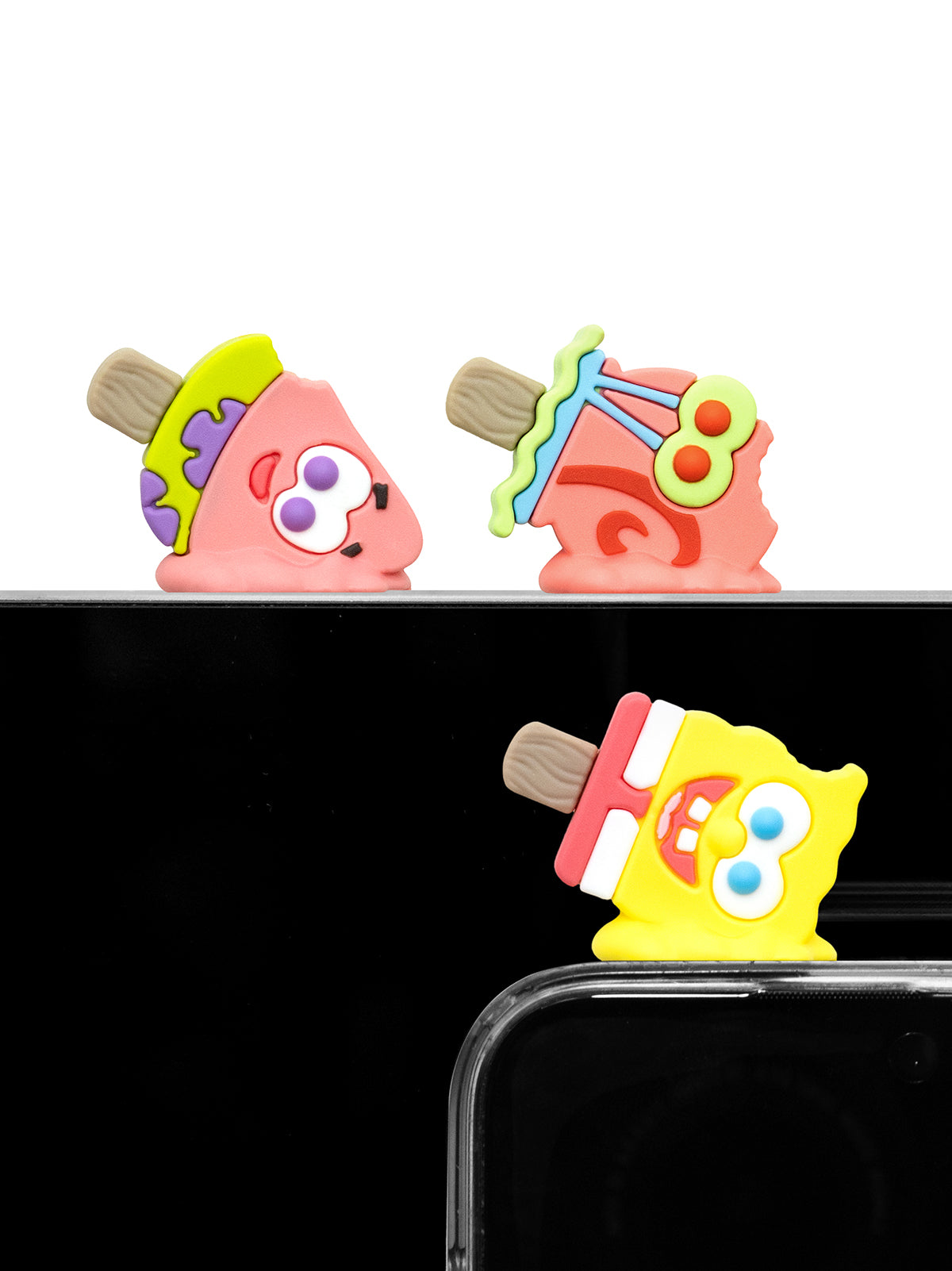Three colorful novelty phone accessories shaped like cartoon characters, shown attached to the top and bottom edges of a smartphone against a black background.