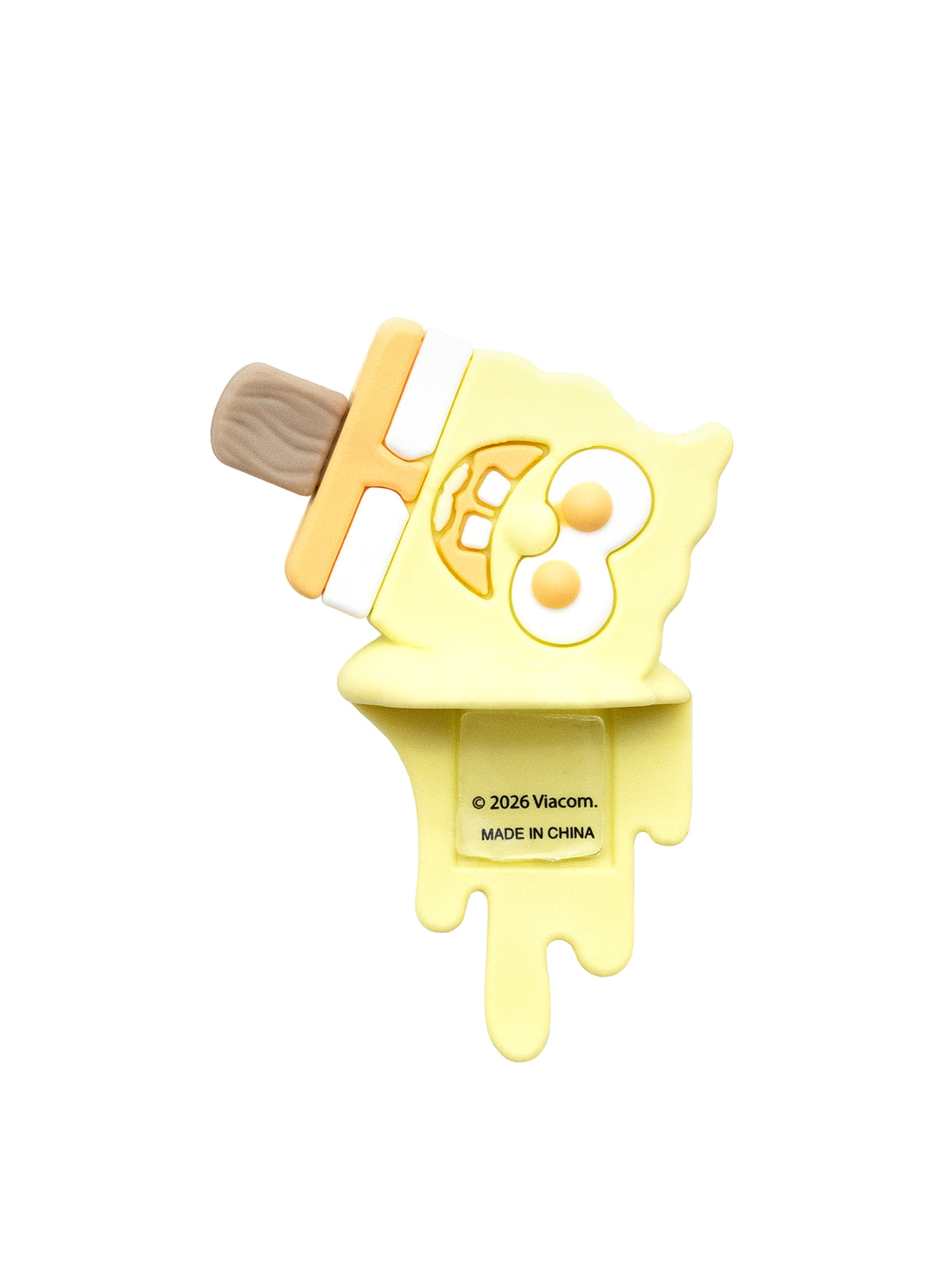 A yellow popsicle-shaped silicone accessory with a cartoon face and a brown stick, shown on a plain white background.
