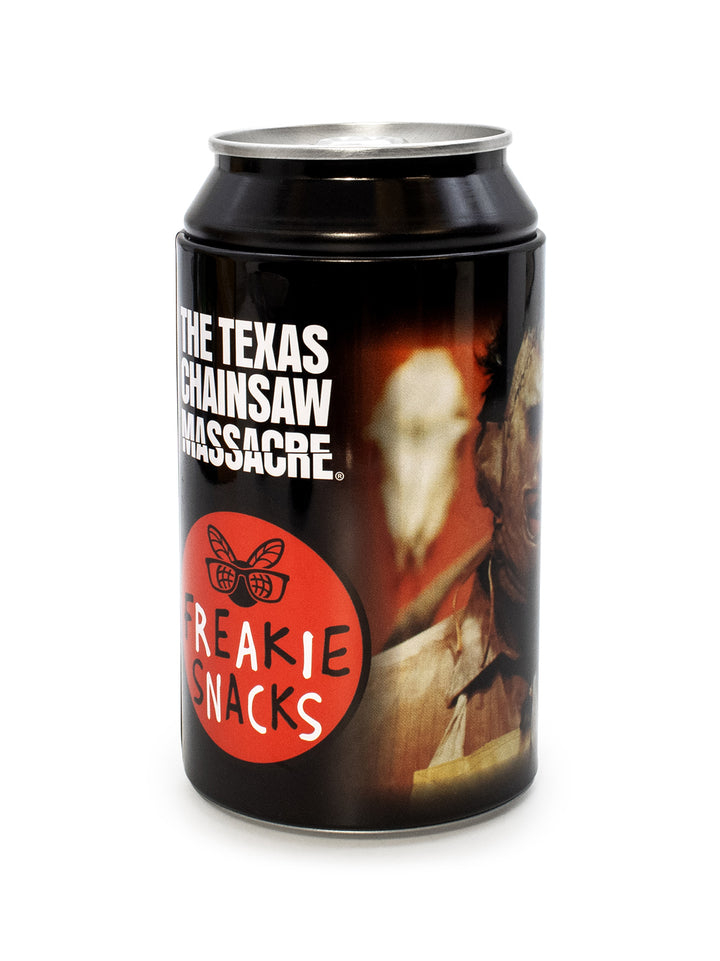 A black metal beverage can with a printed horror-themed label featuring the text 'THE TEXAS CHAINSAW MASSACRE' and a red circle with 'FREAKIE SNACKS' and a bee logo, photographed on a white background.