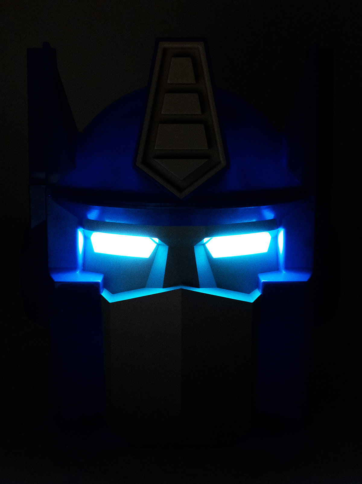 A dark blue Transformers Optimus Prime style helmet or headpiece with glowing bright blue LED eyes, shown against a black background.