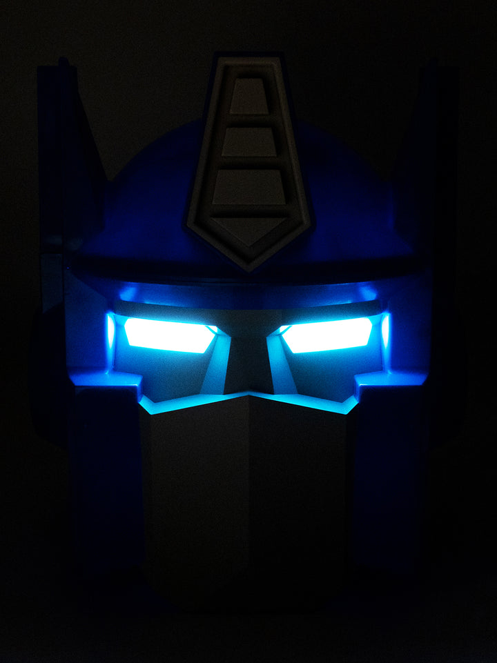 A dark blue Transformers Optimus Prime style helmet or headpiece with glowing bright blue LED eyes, shown against a black background.