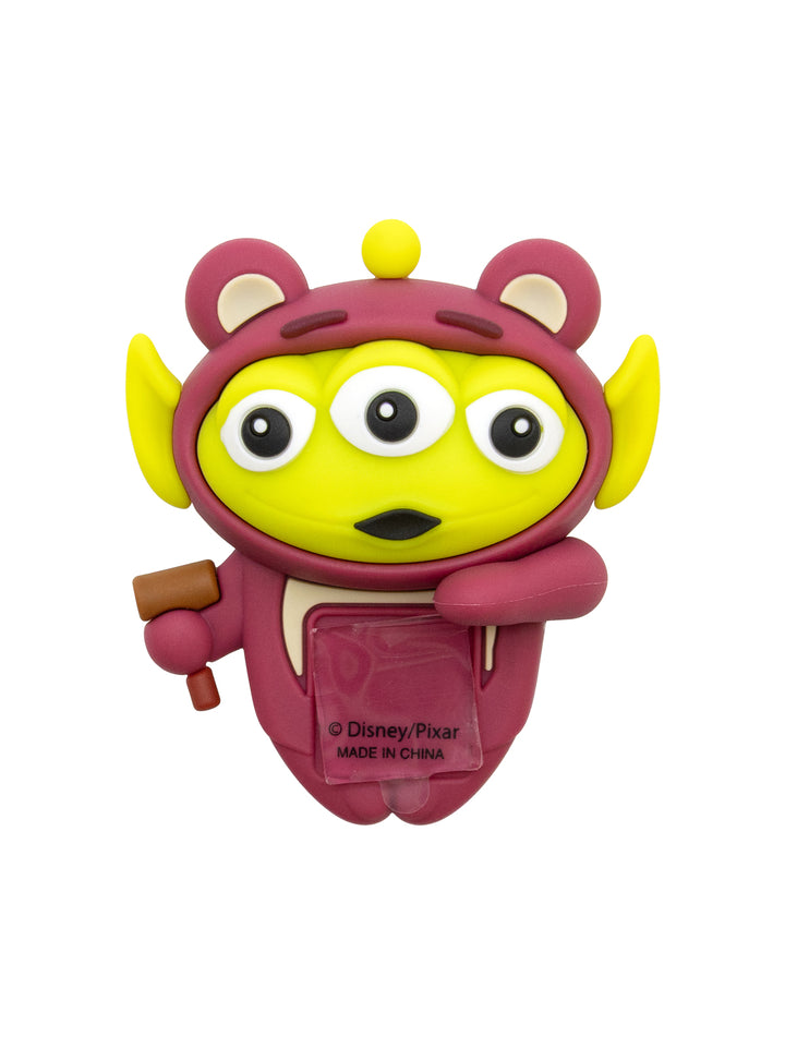 A Disney/Pixar Toy Story Alien figure shaped like the character, featuring a yellow body, pinkish-purple hood and suit, and holding a small brown tool, on a plain white background.