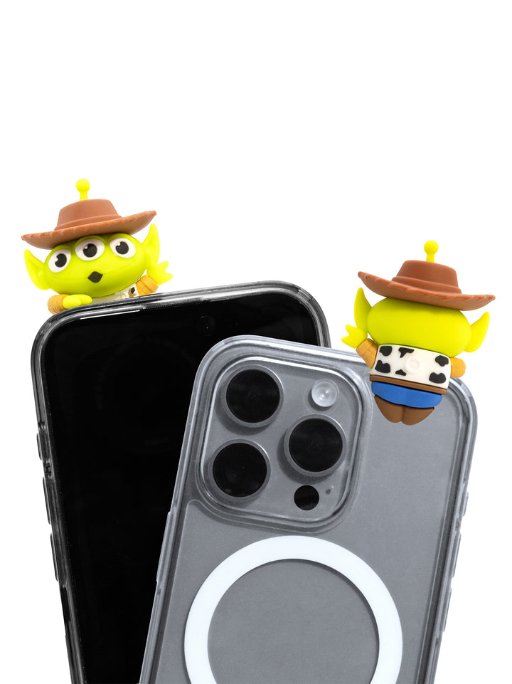 Two small yellow cartoon character phone accessories with brown hats are shown attached to the top corners of two smartphones, one black and one gray, on a plain white background.