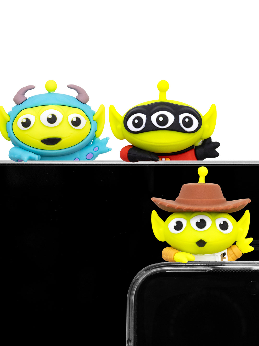 Three small cartoon toy figures resembling alien characters, shown from the back above a black surface. One is blue and gray, one is yellow with black and red, and one is yellow wearing a brown hat.