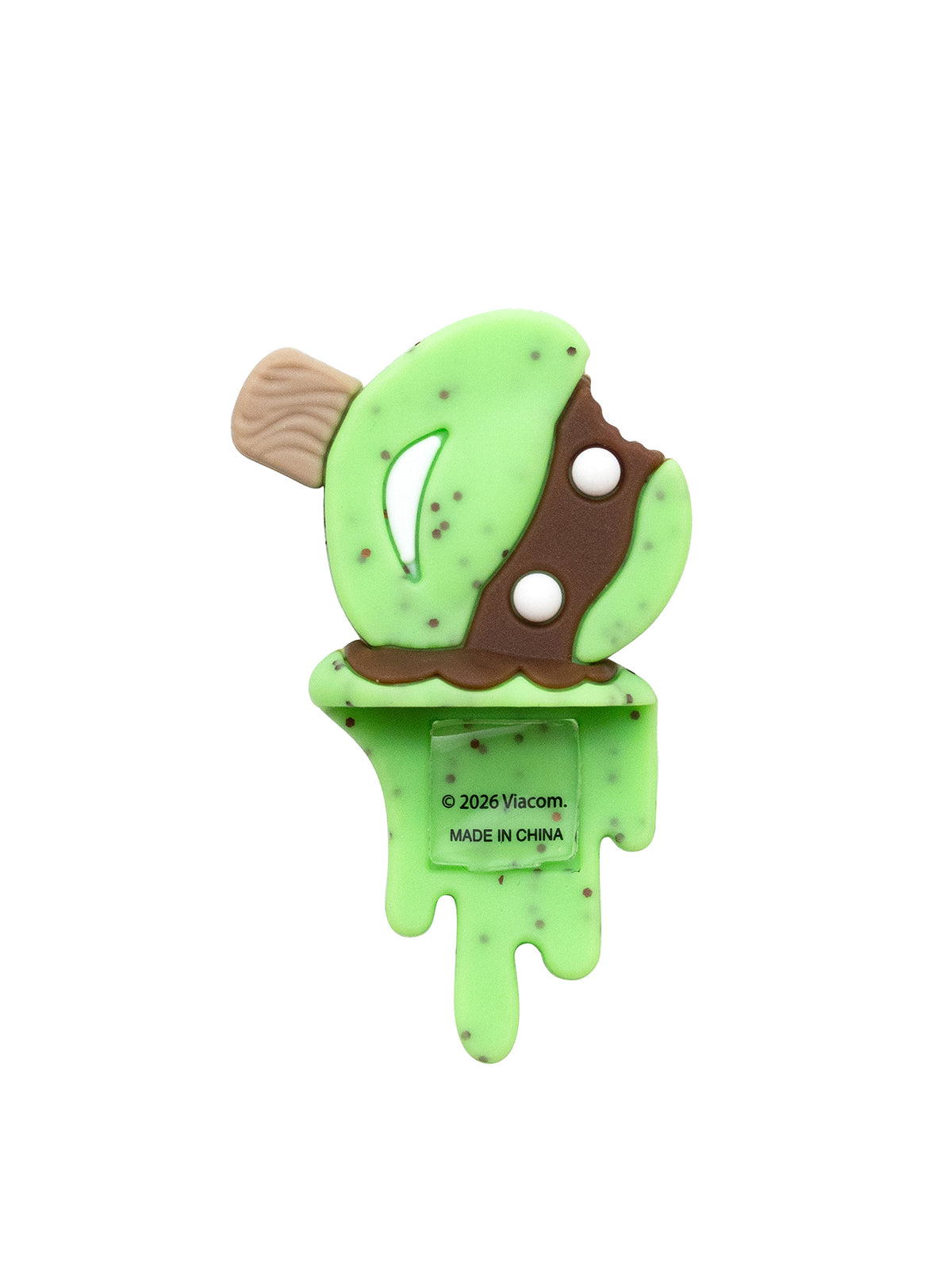 A novelty ice cream cone-shaped figure featuring a green lime-textured top with brown speckles, a brown chocolate drizzle, and a light brown wooden stick, shown on a plain white background.