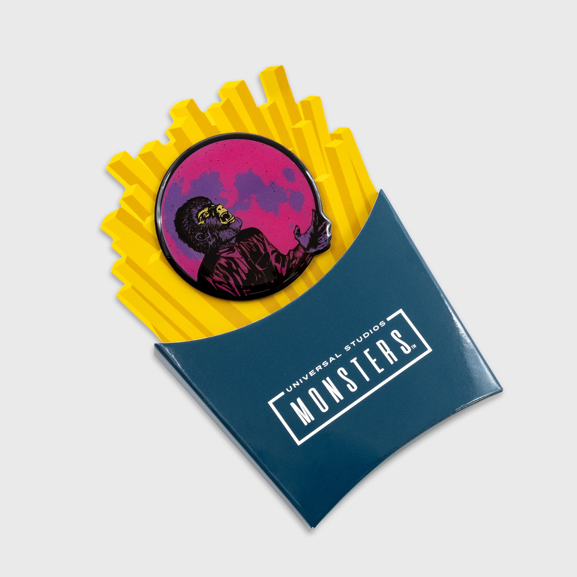 the wolfman enamel pin. on top of french fries packaging. text: universal studios monsters