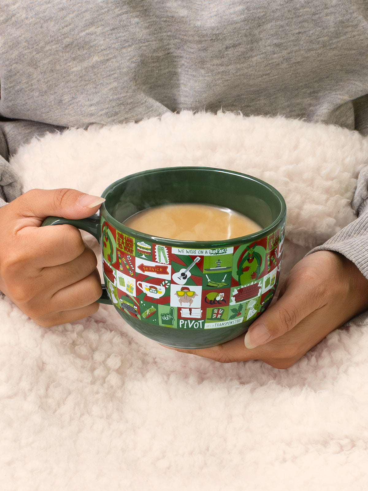 Person holding a green mug with festive design on a soft surface
