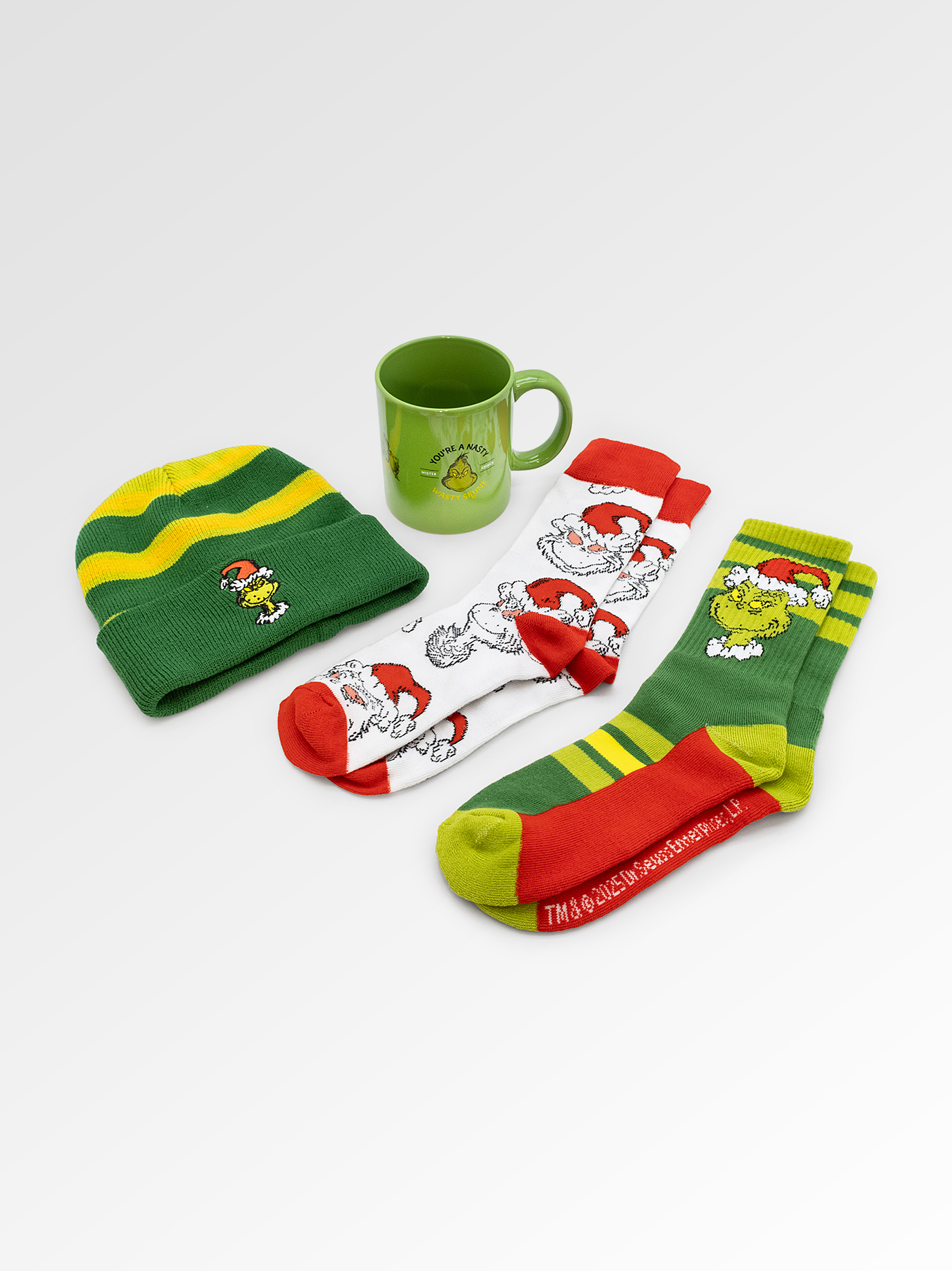 Set of green and red Christmas-themed socks, a beanie, and a mug on a white background