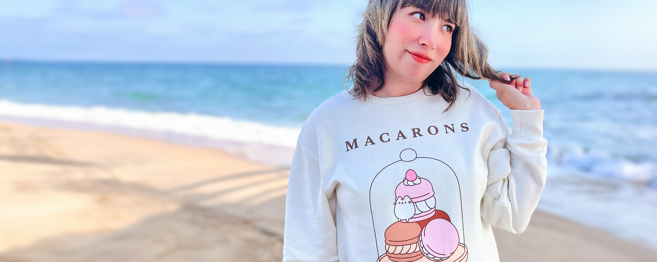 Person wearing a sweatshirt with 'Macarons' design on a beach