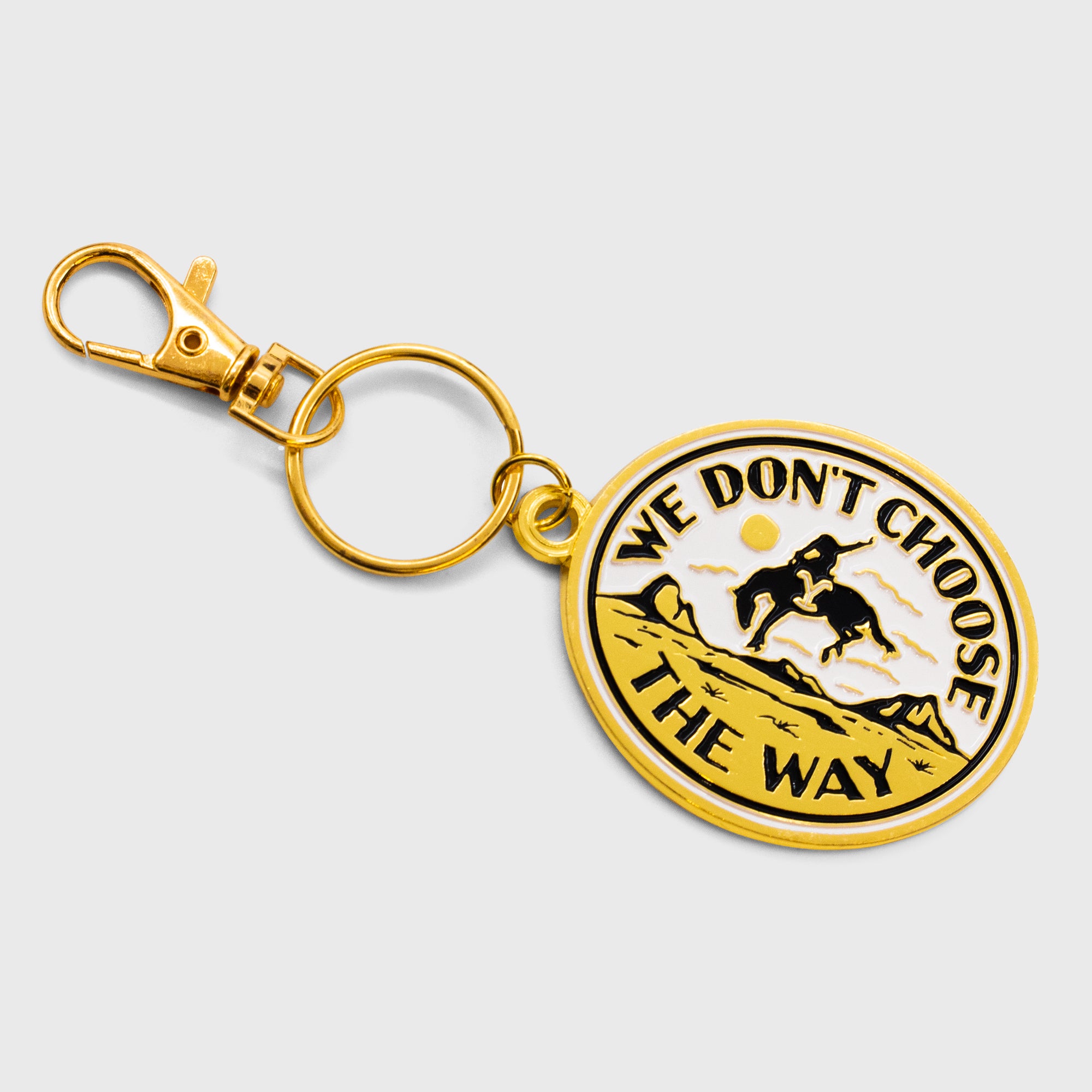 gold texture yellowstone keychain. image: cowboy on horse in desert with mountaints. text: we don't choose the way